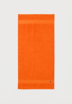 Toalla rectangular de color naranja brillante con tejido texturizado y estrechas bandas horizontales en la parte superior e inferior, pequeño logo oscuro en el borde inferior.
