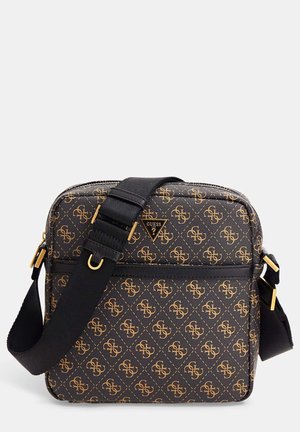 Sac bandoulière Guess à motifs noirs et bruns avec une sangle noire réglable et des accessoires dorés, posé sur un fond clair uni.