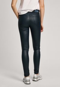 Vaqueros pitillo de cintura alta de color azul oscuro con una textura lisa y brillante; dos bolsillos traseros y detalles mínimos de costuras. Combinados con zapatos deportivos plateados.