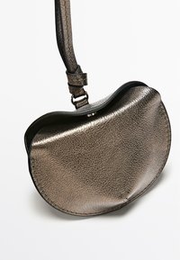 Metaliczna skórzana torebka o zaokrąglonym kształcie, z teksturowaną powierzchnią i smukłym paskiem. Kolor to stonowany brąz.