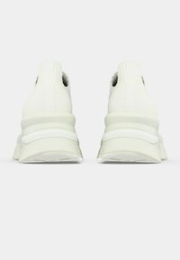 Λευκά αθλητικά παπούτσια με υφασμένο άνω μέρος με υφή, ελαστική θηλιά στη φτέρνα, παχιά λαστιχένια σόλα και σχεδιασμό με στρώσεις. Καθαρή και μινιμαλιστική αισθητική.