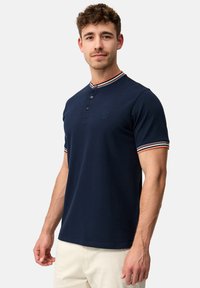Marineblå polo shirt med knaplukning, ribbet rund hals med røde og hvide striber samt logodetalje på brystet. Glat bomuldsstof.