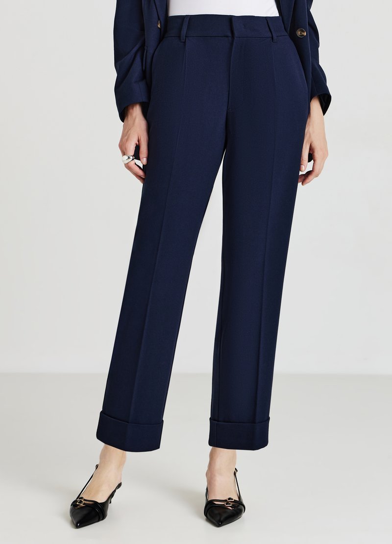 Pantaloni navy su misura con taglio dritto, rifiniture alle caviglie, pince frontali e una finitura in tessuto liscia. Abbinati a scarpe nere a punta.
