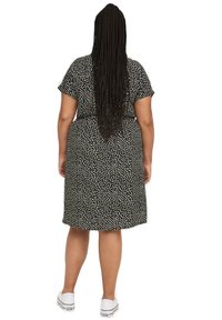 Robe noire avec un motif à taches blanches, à manches courtes, longueur genoux et coupe ample. Portée avec des baskets blanches. Tissu texturé.