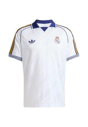 Bela nogometna majica z modrim ovratnikom, rumenimi in modrimi črtami na rokavih, logotipom Adidas na levi strani prsnega koša in grbom Real Madrida na desni strani prsnega koša.