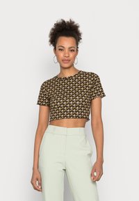 Brown crop top with a repeating patterned design in yellow and green; short sleeves and a round neckline, paired with light green trousers.