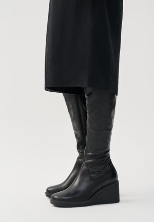 Schwarz lederne kniehohe Stiefel mit Keilabsatz, ausgestattet mit einer glatten Oberflächenstruktur und einem seitlichen Reißverschluss. Entworfen mit einer schlanken, körperbetonten Silhouette.