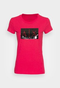 Camiseta de manga corta rosa con un parche rectangular de lentejuelas negras y plateadas que presenta las letras "A|X" en rojo en el centro. Tejido texturizado.