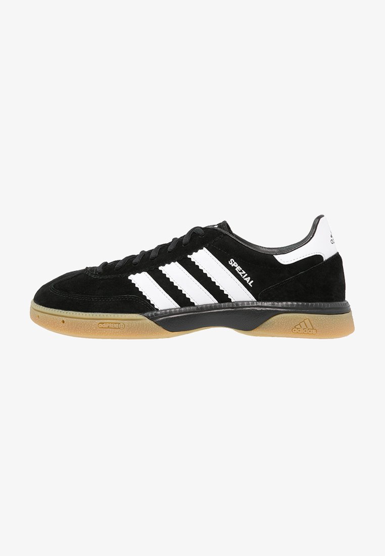 Sneaker em camurça preta com três riscas brancas, sola em borracha creme e detalhes em preto. Apresenta um perfil baixo e um design de bico redondo.