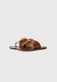 Brune lærsandaler med flad sål, åbent tådesign og dekorativt hardware på remmene. Glat tekstur, minimalistisk stil.
