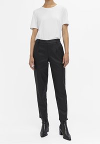 Casual wit t-shirt met korte mouwen, gecombineerd met high-waisted zwarte broek. Zwarte enkellaarsjes maken de outfit compleet. Eenvoudig, strak ontwerp.