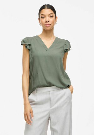 Blusa verde oliva con escote en V y mangas cortas con acentos fruncidos. Textura suave, corte holgado, combinada con pantalones gris claro.