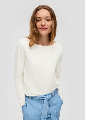 Witte lange mouwen top gemaakt van een gladde, lichte stof, gecombineerd met lichtblauwe high-waisted broeken met een gestrikt riemdetail.