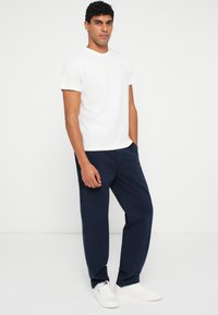 Λευκό βαμβακερό μπλουζάκι με στρογγυλή λαιμόκοψη, συνδυασμένο με ναυτικά μπλε παντελόνια και λευκά αθλητικά παπούτσια με διακριτικά λογότυπα.