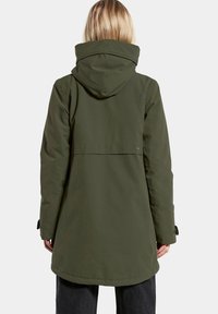 Parka impermeable de color verde oliva con capucha, diseño ligeramente ajustado y puños elásticos. Cuenta con una ventilación en la parte trasera y un logotipo discreto en el hombro.