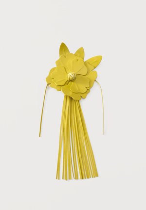 Fleur en cuir jaune avec des pétales superposés, trois formes de feuilles, un centre noué et de longs pompons à franges qui pendent vers le bas.