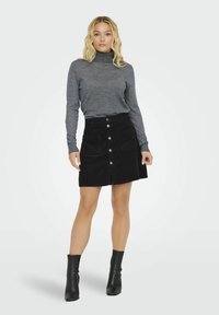 Melna korduroja svārku ar priekšējiem pogām, sānu kabatām un izplūdušu apakšmalu, kombinēta ar pelēku turtleneckreklu un melnām potīšu zābaciņiem.