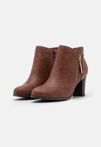 Bottes basses en similicuir marron avec un bout arrondi, des fermetures éclair latérales et un talon carré. La texture est lisse avec un grain subtil.