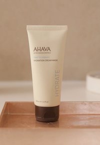 Máscara hidratante AHAVA en un tubo beige claro con una tapa marrón, etiquetada "ES HORA DE HIDRATAR" y "HIDRATAR", tamaño de 100 ml.