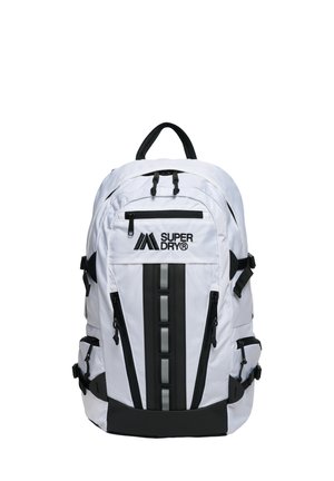 Sac à dos Superdry blanc avec fermetures éclair noires, bande réfléchissante verticale, plusieurs compartiments et poignée supérieure rembourrée.