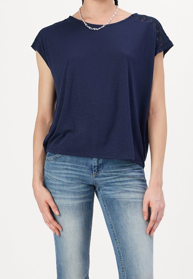 Haut à manches courtes bleu marine avec une texture douce et des accents de dentelle sur les épaules, associé à un jean ajusté bleu clair.