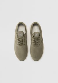 Oliwkowe sportowe buty z dzianinowej cholewki, z wiązaniem, wyściełanym językiem i białą gumową podeszwą. Posiadają logo na języku.