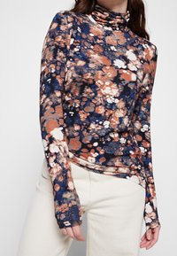 Langarm-Turtleneck-Oberteil mit einem abstrakten Muster in Marineblau, Orange und Creme. Hergestellt aus einem weichen, elastischen Stoff mit einer taillierten Passform.