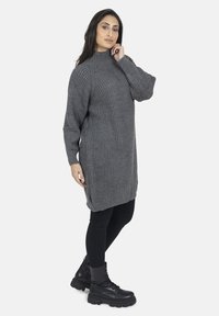 Grå ribbet strikkjole med høj hals, lange ærmer og sideslids, parret med sorte skinny jeans og snørelukning kampstøvler.