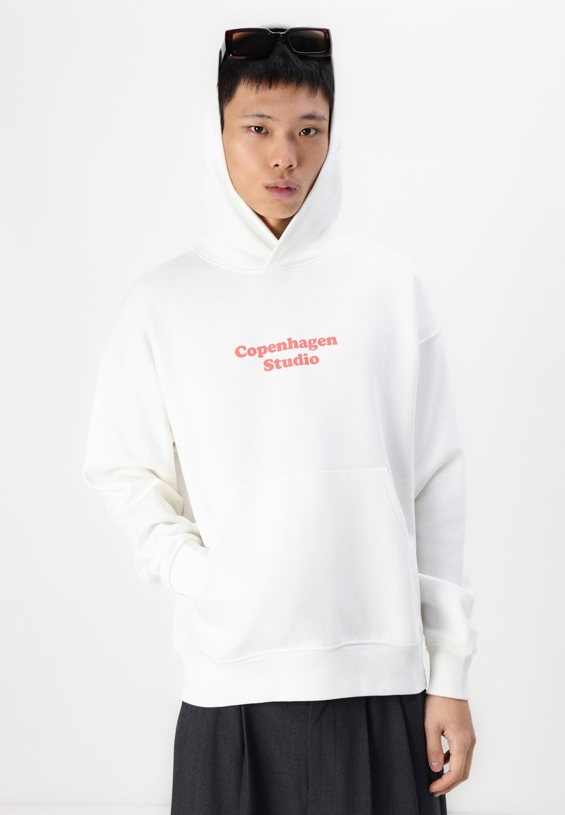 Witte hoodie met een voorzak, voorzien van "Copenhagen Studio" in het rood gedrukt. Glad materiaal met een aansluitende capuchon en geribde manchetten.