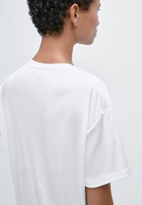 Witte katoenen t-shirt met een ronde hals, korte mouwen en een losse pasvorm; de achterkant heeft een gladde textuur zonder zichtbare patronen.