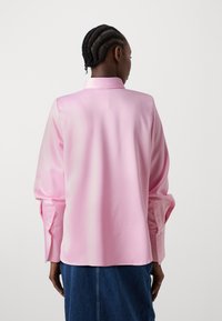 Lyserød satinbluse med krave og knapforsynede manchetter. Har lange ærmer og en glat tekstur, der hænger elegant bagpå.