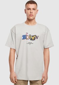 Lys grå kortærmet t-shirt med et flerfarvet "BKLYN" grafik på fronten og tekst nedenfor. Simpel, afslappet pasform med en glat tekstur.