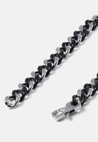 Pulseira de corrente preta e prateada com elos entrelaçados, apresentando resina preta suave e realces de metal polido, fixada por um fecho.