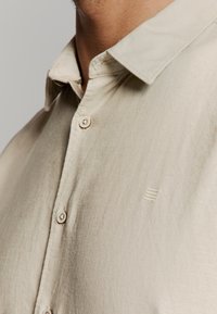 Beige overhemd met knopen, gemaakt van een licht gestructureerde stof, voorzien van een kraag en een klein logo op de borst. Licht gestructureerd ontwerp.