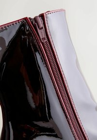 Glansende sorte ankelstøvler med en bordeaux lynlås. Har en glat lakoverflade, afrundet design og kontrasterende syninger langs lynlåsen.