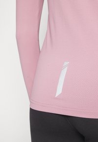 Långärmad rosa topp i en texturerad tyg, med en vit detalj vid fållen. Kombinerad med svarta leggings som betonar en tight passform.