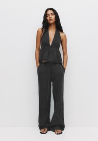 Haut à bretelles noir texturé avec un décolleté en V profond, associé à un pantalon large, doté d'une taille élastique et de poches latérales. Sandales minimalistes.