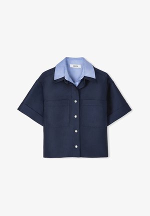 Námořnická košile s krátkým rukávem a světle modrým límečkem, která má dvě přední kapsy a stříbrné zapínání na knoflíky. Hladká textura látky.