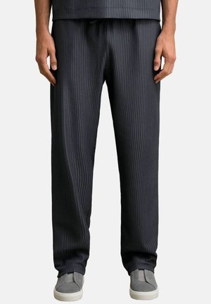 Pohodlné tmavošedé pruhované nohavice s elastickým pásom a voľným strihom, skombinované so šedými nazúvacími topánkami.