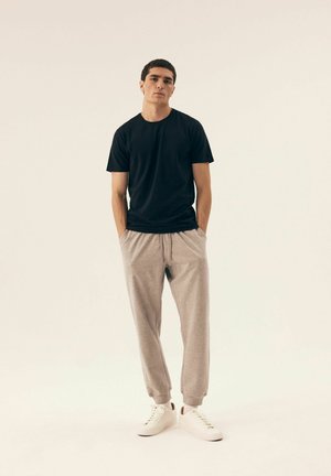 Schwarzes Kurzarm-T-Shirt und hellgraue Jogginghose, aus weichem Stoff, mit einem elastischen Bund und legerem Schnitt, dazu weiße Sneakers.