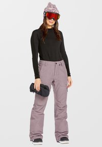 Conjunto de esquí que incluye una camiseta ajustada de manga larga negra, pantalones de esquí morados claros con bolsillos y botas de nieve negras con detalles en plata; sosteniendo guantes.