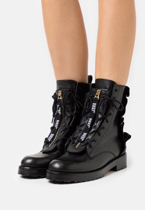 Bottes en cuir noir montantes, avec fermetures éclair dorées, lacets en ruban et semelle robuste. Coutures détaillées sur les côtés et design à lacets.