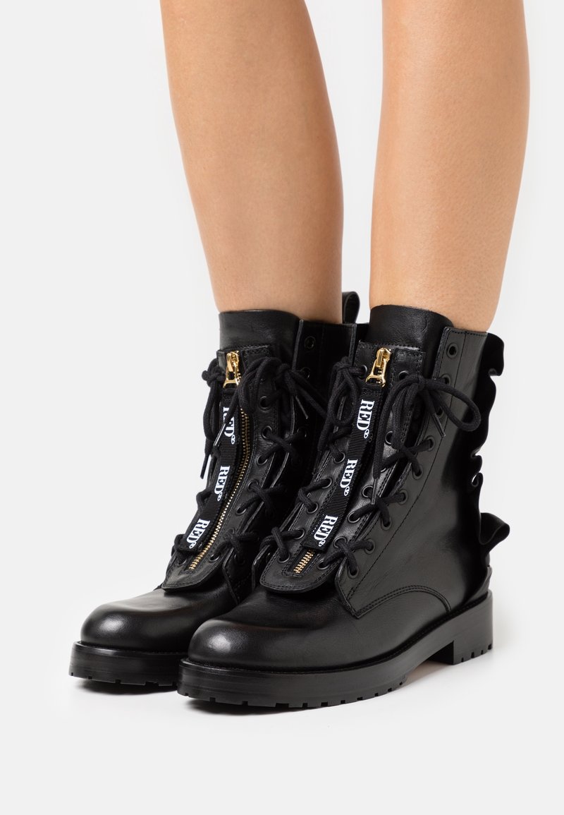 Bottes en cuir noir montantes, avec fermetures éclair dorées, lacets en ruban et semelle robuste. Coutures détaillées sur les côtés et design à lacets.