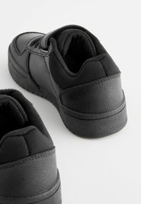 Baskets de sport noires avec une tige synthétique lisse, un col rembourré et des semelles en caoutchouc texturé. Présente un design bas avec des lacets.