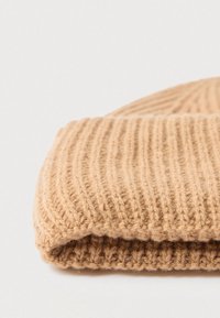 Helepruun kudumismüts sooniliste detailidega. Omab serva, mis on üles keeratud, ja pehmet villataolist materjali.