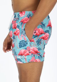 Blue swim shorts featuring a vibrant pink flamingo and tropical leaf pattern, made of lightweight material with an elastic waistband.