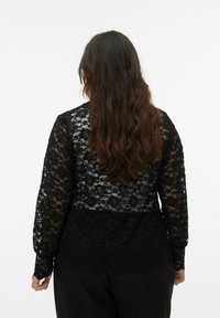 Zwarte kanten top met lange mouwen, met bloemmotieven en een golvende zoom. Achteraanzicht toont een gestructureerde stof en een gelaagd ontwerp.