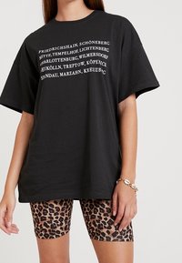 Camiseta oversized negra con texto blanco que enumera los distritos de Berlín. Combinada con pantalones cortos de ciclismo de estampado de leopardo, con un diseño ajustado.