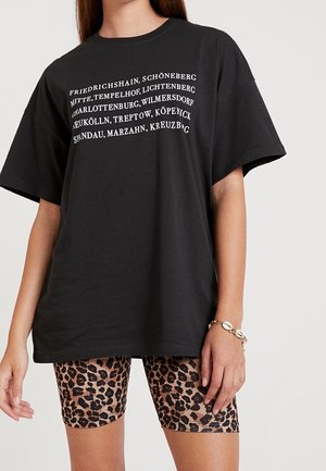 Czarna, oversize koszulka z białym napisem wymieniającym dzielnice Berlina. Połączona z szortami rowerowymi w leopardzi wzór o dopasowanym kroju.