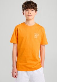 T-shirt in cotone arancione con collo rotondo e maniche corte, dotato di una grafica bianca sul lato sinistro del petto. Tessuto liscio.